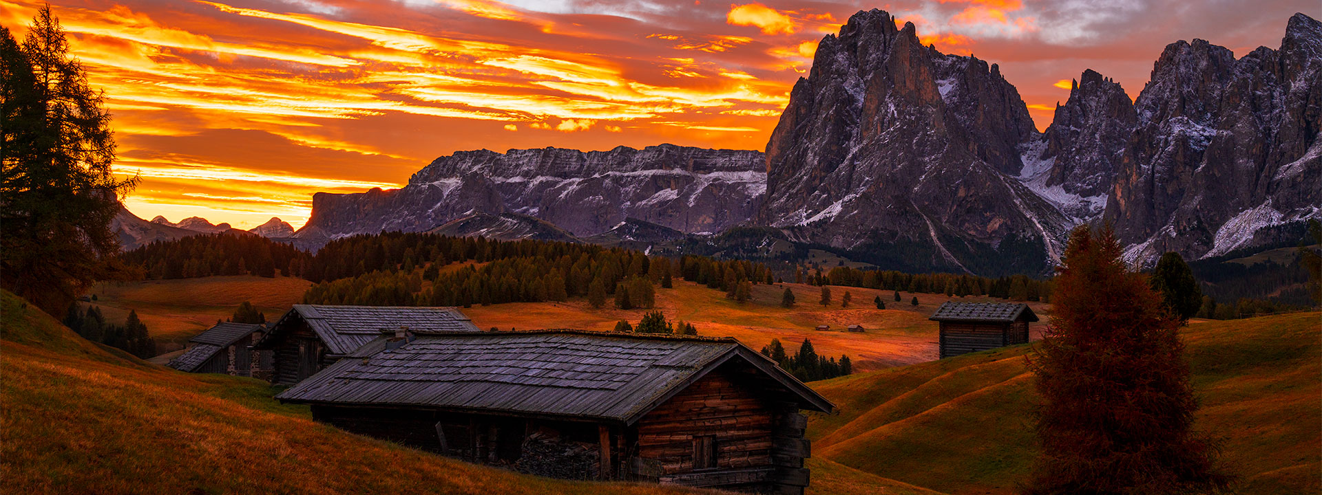 Sunrise light on sharp mountain peaks in the Dolomites with alpine huts in the foreground.